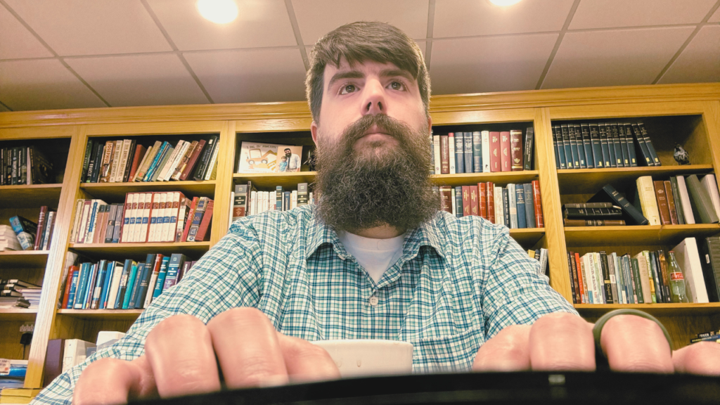 A man wearing a green checked shirt sitting at a desk typing on a keyboard.
